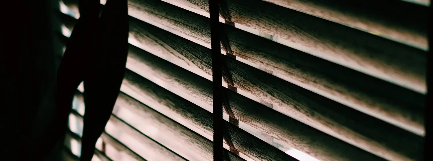 Lamas de una persiana de madera en penumbra con luz entrando por detrás