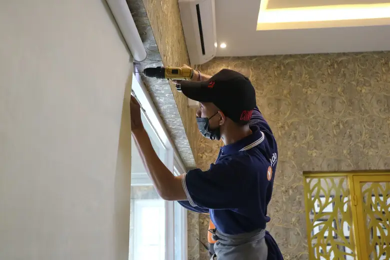 Operario con un taladro instalando un soporte junto a la ventana de una vivienda