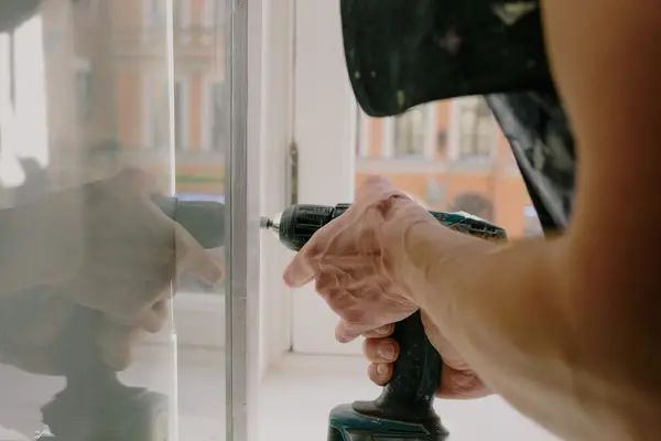 Manos de un operario atornillando una ventana con un taladro, igual que en una reparación a domicilio en Pamplona