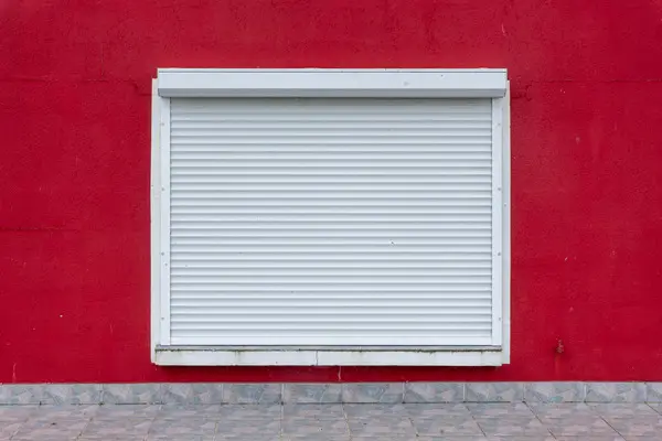 Persiana enrollable blanca cerrada sobre una ventana de pared roja, el tipo de avería que atendemos en Pamplona